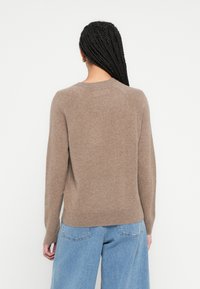 Καφέ πλεκτό πουλόβερ με μακριά μανίκια, στρογγυλή λαιμόκοψη και ριμπ τελείωμα. Η υφή φαίνεται μαλακή, με ομαλή επιφάνεια. Καθημερινό σ�χέδιο, συνδυασμένο με τζιν.