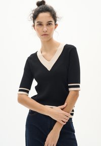 Schwarzer gerippter Strickpullover mit einem beigen V-Ausschnitt und gestreiften Bündchen. Hat kurze Ärmel und einen figurbetonten Schnitt.