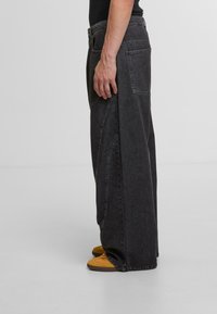 Black denim trousers with a relaxed fit, featuring a unique curved seam design. Details include a back pocket and a high waist.