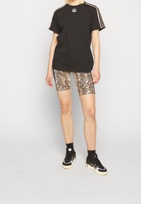 Czarny bawełniany T-shirt z białym logo, w połączeniu z błyszczącymi szortami rowerowymi w wężowy wzór. Czernie sneakersy z białymi akcentami dopełniają całość.