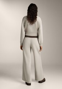 Svetlo siva pletena majica s teksturom i široke trenerke s smešnim pojasom. Mekani materijal s opuštenim krojem, naglašen rebrastim dizajnom.