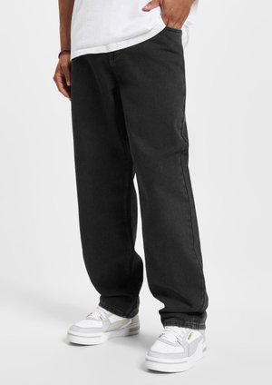 Sorte rettlagejeans med en glatt tekstur og subtile sømdetaljer, sammen med hvite sneakers med grå accenter.