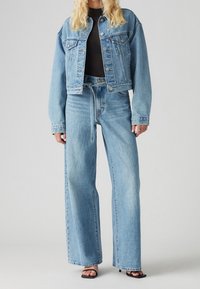 Denimjacka och vida jeans i ljusblått. Jackan har framfickor och knappstängning, medan jeansen har elastisk midja med dragsko och en lätt blekning.