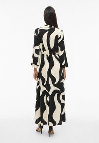 Dolga, sproščajoča obleka z črno-bež valovitim vzorcem, ki ima dolge rokave in elastičen pas, izdelana iz lahkotnega materiala.