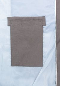 Poche rectangulaire en tissu gris avec couture visible cousue sur un fond en tissu bleu clair, avec un rabat en tissu dépassant au-dessus de la poche.
