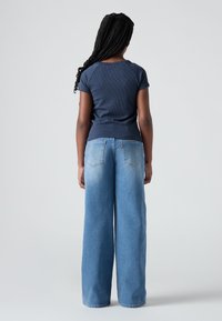 Ναυτικό ριγέ κοντομάνικο μπλούζα συνδυασμένη με ανοιχτό μπλε φαρδύ παντελόνι τζιν που διαθέτει πίσω τσέπες και διακριτική κλιμάκωση ξεθωριάσματος.