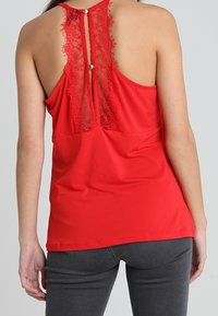 Rode mouwloze top met een kanten rugdetail met knoopsluiting, gemaakt van een zachte stof, met een aansluitend ontwerp en een gladde textuur.