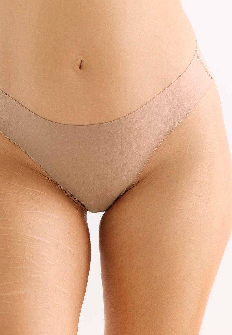 Nude naadloze bikini onderkant van gladde stof, met een lage taille en een minimalistisch ontwerp. Subtiele glans en zachte textuur.
