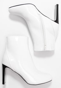 Weiße Lackleder-Ankle-Boots mit sleekem Design, spitzer Zehenform und hohem schwarzen Stiletto-Absatz, ausgestattet mit einem seitlichen Reißverschluss.
