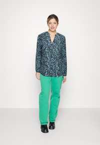 Mørkeblå og turkismet mønstrete bluse med lange ermer, kombinert med lysegrønne bukser. Outfiten har en avslappet passform og en V-hals design.