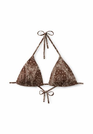 Frau trägt braunes gemustertes Bikini und rechteckige Sonnenbrille, richtet die Sonnenbrille mit einer Hand vor hellem einfarbigem Hintergrund.