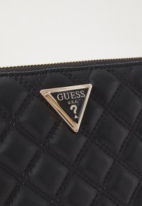 Czarny pikowany portfel z faux skóry z srebrnym trójkątnym logo "Guess U.S.A." z znakiem zapytania, złotymi akcentami i zamknięciem na zamek.