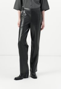 Zwarte faux leren broek met een slanke, rechte snit. Hoge tailleband met drukknoopjes. Gladde, glanzende textuur. Gekocht met zwarte hakken.