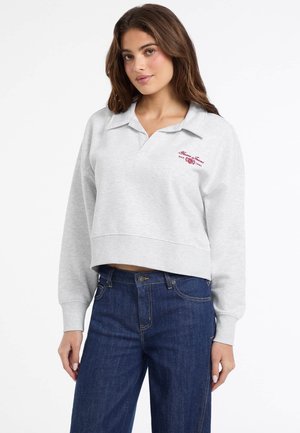 Sweatshirt gris court avec un col polo et un logo rouge brodé. Assorti avec un jean en denim bleu foncé. Matériau doux, coupe décontractée.
