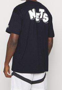 Camiseta de algodón azul marino con la palabra "NETS" en bold letras blancas texturizadas en la parte de atrás. Mangas cortas y corte relajado.