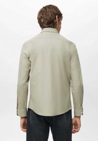 Camisa de manga larga color verde claro con cuello puntiagudo, puños abotonados y dobladillo recto, hecha de tela suave. Vista trasera.