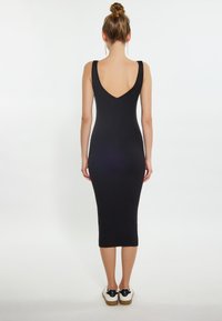 Abito midi nero a coste con scollo a V sul retro, sagomato e con spalline larghe. Indossato con sneakers bianche con dettagli neri.