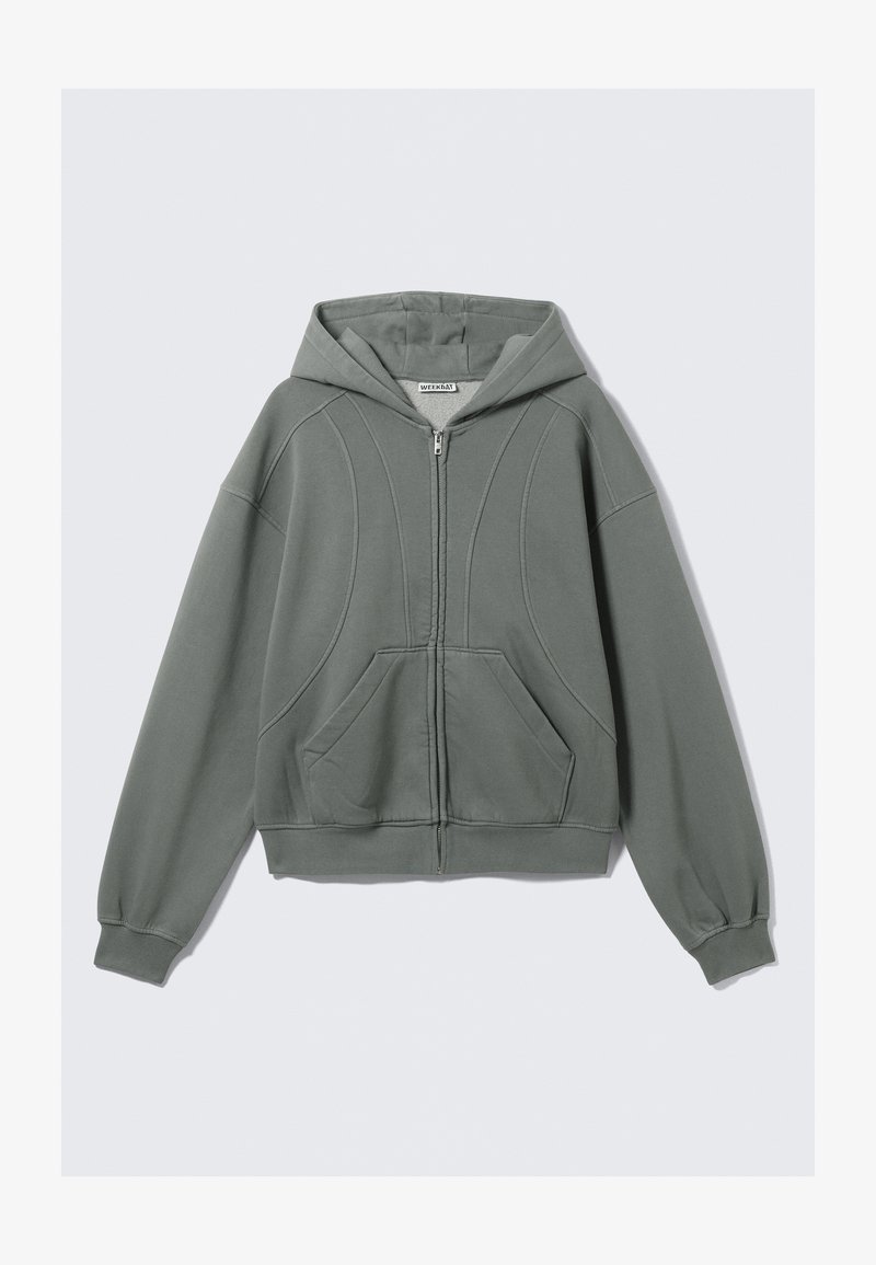 Sweat à capuche zippé gris clair en tissu doux. Il comprend une capuche, deux poches avant et des coutures courbes décoratives. Poignets et ourlet côtelés.