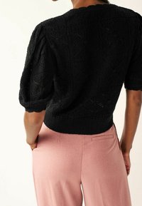 Pullover nero lavorato a maglia con texture a motivo, maniche corte a sbuffo e vita a coste, abbinato a pantaloni tailleur rosa.
