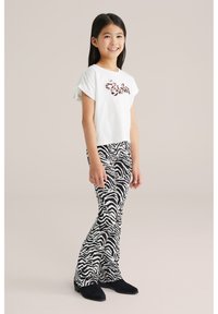 Vit kortärmad t-shirt med "Estela" i leopardmönster, kombinerat med svarta och vita zebramönstrade utsvängda leggings och svarta mockaskor.