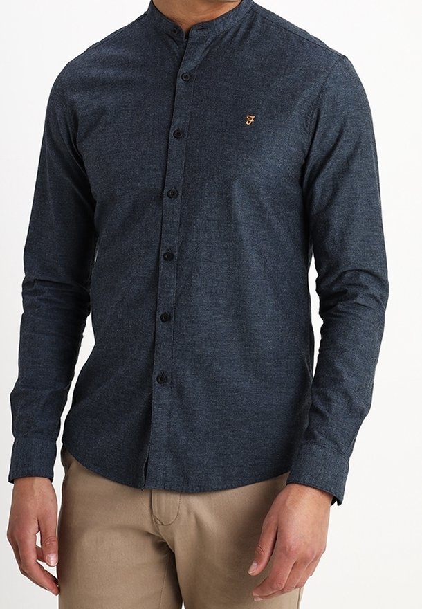 Camisa de botones azul oscuro con cuello mandarín; hecha de tela texturizada; presenta un pequeño logo dorado en el pecho y botones negros.