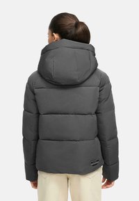 Veste en duvet grise avec une capuche, présentant des sections matelassées et un détail de logo en bas à droite. Le matériau semble lisse et isolant.
