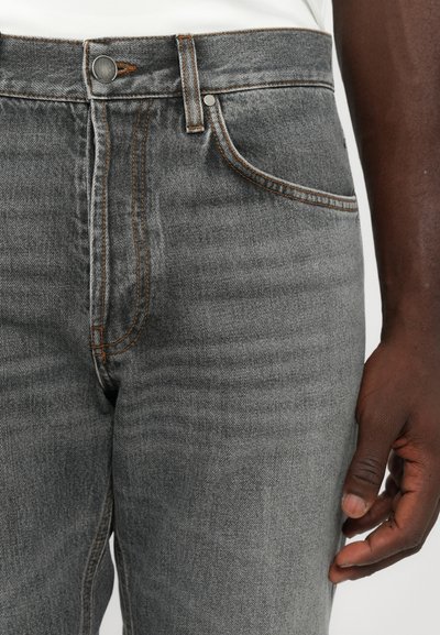 Close-up of person wearing grey denim jeans, showing button, front pocket, stitching details, and one relaxed hand by their side.