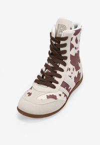 Zapatillas altas en color crema y marrón con estampado de vaca, cordones marrones, material de ante, puntera redondeada y suela de goma con rayas blancas.