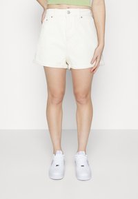 Pantalones cortos de mezclilla blanca con dobladillos enrollados, diseño de cinco bolsillos y cierre frontal con botón. Combinados con zapatillas blancas con acentos morados.