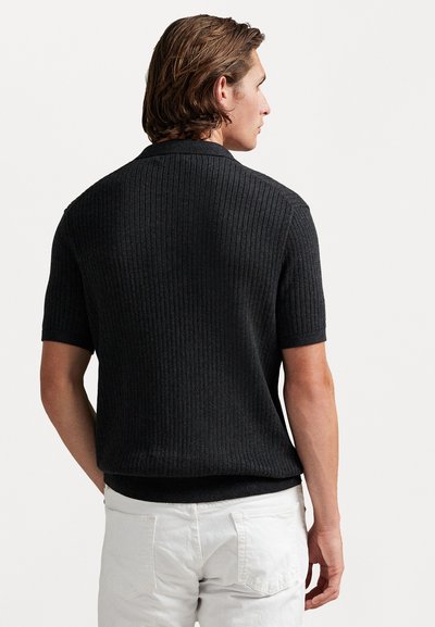 Μαύρος ριχτός πλεκτός πουλόβερ με κοντά μανίκια και υφή. Εφαρμοστή γραμμή με λεία επιφάνεια και ελαφρώς καμπυλωτό στρίφωμα.