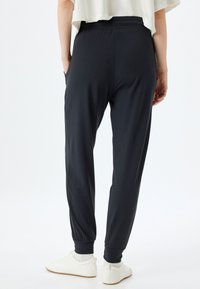 Zwarte joggingbroek gemaakt van zachte stof, met een elastische tailleband, zijzakken en taps toelopende manchetten bij de enkels.