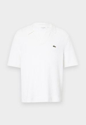 Polo shirt bianco a maniche corte realizzato in tessuto testurizzato. Presenta un colletto a V e un piccolo logo verde sul petto sinistro.