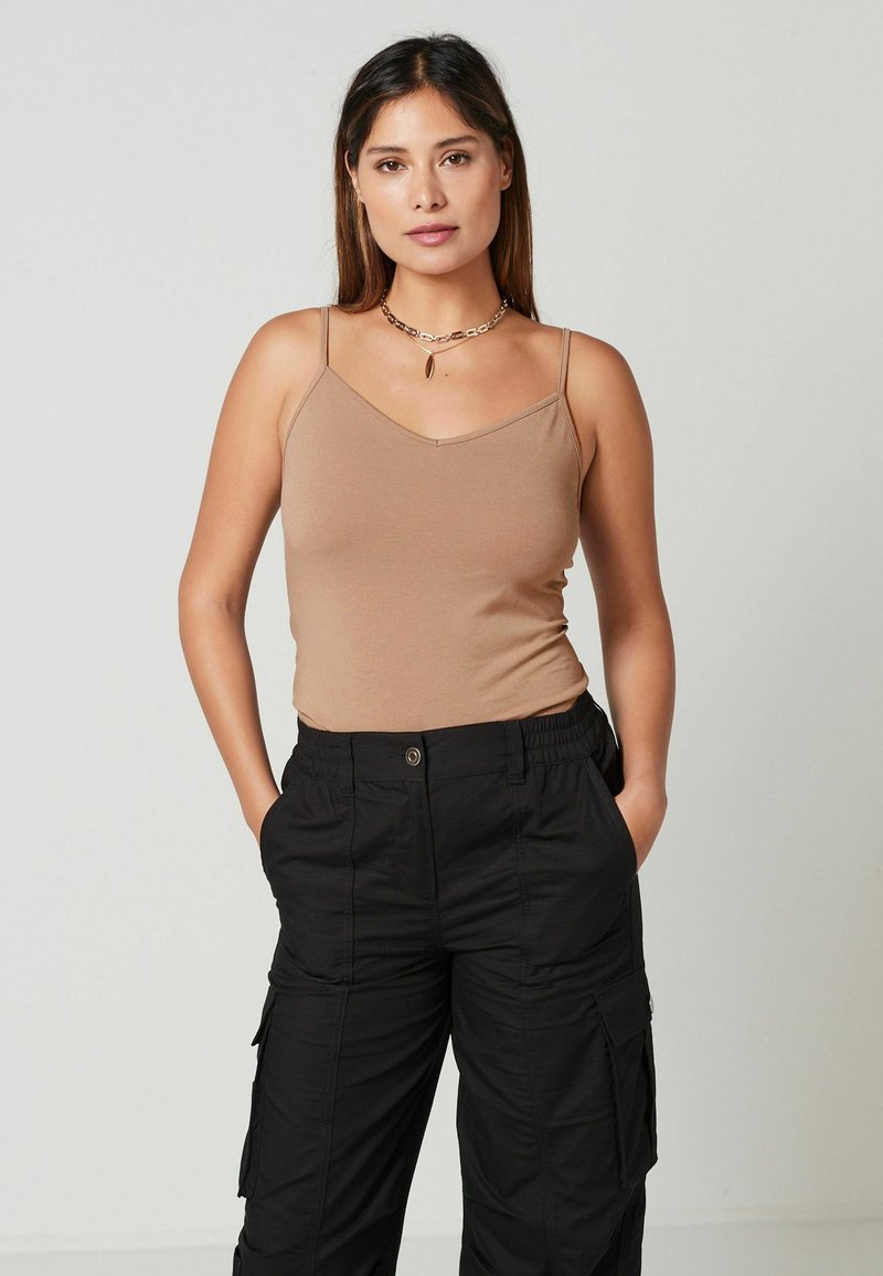 Tan fitted top met dunne bandjes gecombineerd met zwarte cargobroek met een elastische tailleband en meerdere zakken.