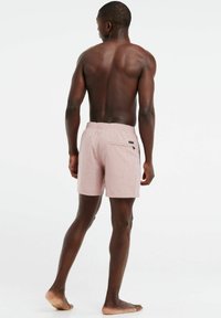 Helle rosa Badeshorts mit elastischem Bund, Gesäßtasche und subtiler Textur, von hinten an einer Person gezeigt.