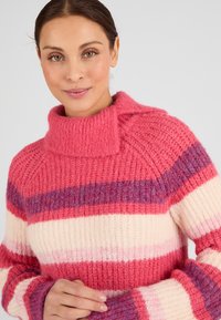 Maglione lavorato a maglia con collo alto, strisce rosa e crema, tessuto a trama e dettagli blu, che mette in evidenza un design spesso.