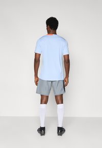 T-shirt de sport bleu clair à manches courtes, associé à un short gris avec un panneau latéral noir et des chaussettes blanches jusqu'aux genoux.