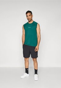 Grønn ermeløs treningsskjorte, svarte shorts, hvite joggesko og svarte sokker. Stoffet virker glatt; har en logo på skjorten.