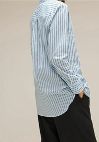 Ljusblå randig skjorta med långa ärmar, knappmanschetter och en avslappnad passform. Har vertikala marinblå ränder och en detalj vid ryggen.