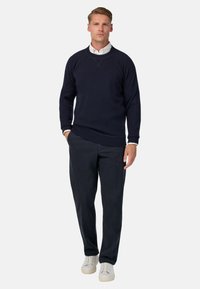 Jersey de cuello redondo azul marino con puños de canalé, combinado con pantalones gris oscuro y zapatillas blancas, que presenta una textura suave y un diseño sencillo.