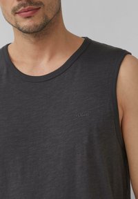 Tumedat hallid ilma varrukateta topp, mis on valmistatud pehmest kangast. Omab ümmargust kaelust ja väikest logo kergelt heledamas varjus rinnal.