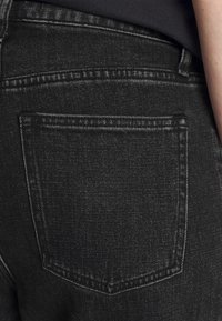 Jeans in denim nero con una tasca posteriore con cucitura doppia e una texture sottile. Il tessuto ha una leggera lucentezza.