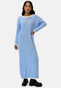 Hellblaues, geripptes Strickkleid mit langen Ärmeln, weiter Halslinie und kontrastierendem weißen Besatz an Bündchen und Saum. Kombiniert mit schwarzen Knöchelstiefeln.