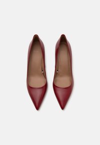 Červené kožené stiletto boty s špicatou špičkou, hladkým povrchem a jednoduchým designem. Interiér má světlé béžové stélky.