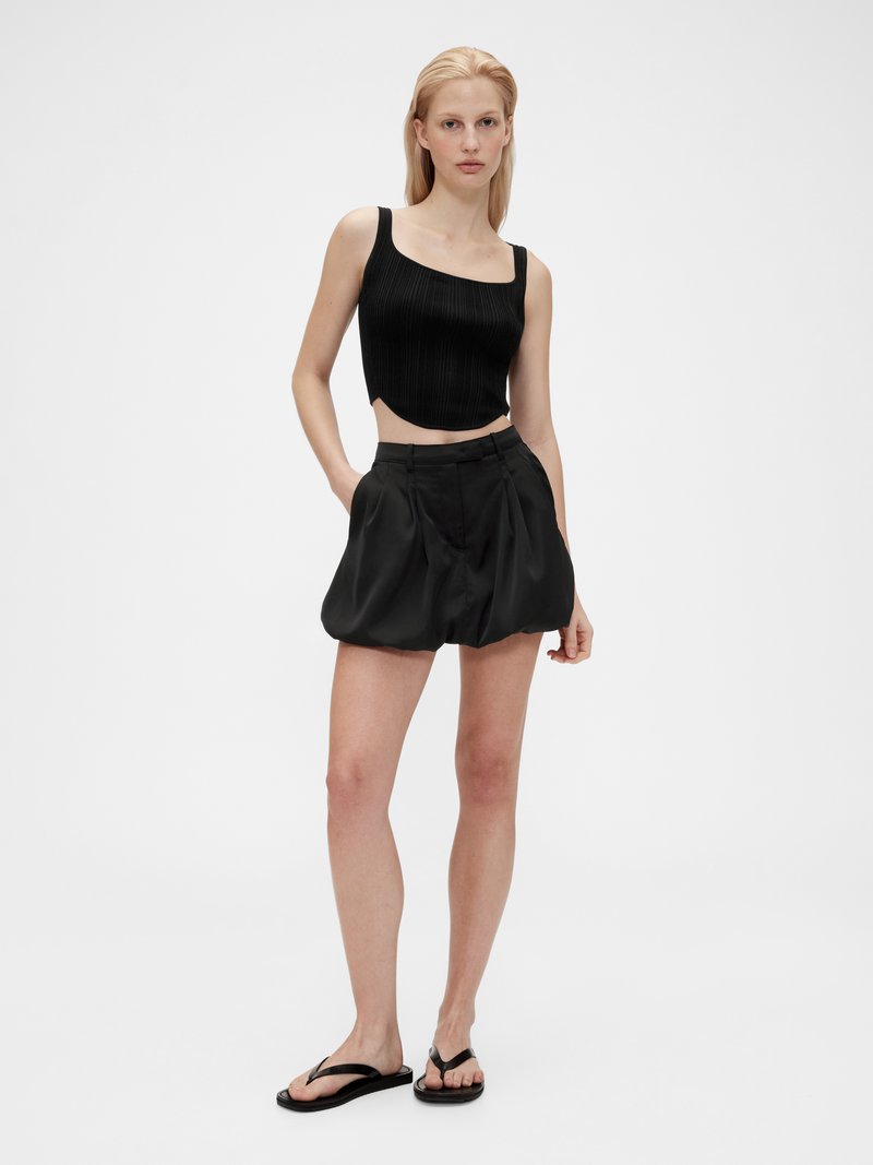 Svart ribbad crop top med rak halsringning, matchad med lösa svarta shorts med en mjuk yta och sidofickor. Enkla svarta flip-flops.
