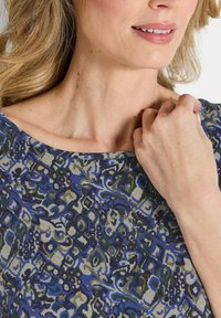 T-shirt à manches courtes, col rond, présentant un motif floral multicolore dans des nuances de bleu, vert et crème sur un tissu texturé.