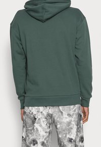 Groene hoodie met een ontspannen pasvorm, ribgebreide boorden en zoom. Gekocht in combinatie met lichtgrijze, gemarmerde broek met zakken.