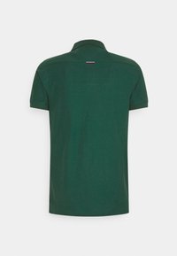 Polo shirt court vert foncé montré de dos avec un petit détail brodé rouge et blanc sous le col.