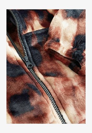 Hnědá a černá fleecová bunda s vzorem, černým zipem a texturou tkaniny. Blízký záběr ukazuje měkký, nadýchaný materiál a výraznou barevnost.