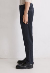 Navy Corduroyhosen mit geradem Schnitt, strukturiertem Stoff, seitlichen Taschen und dezentem Detail an den Gesäßtaschen, kombiniert mit schwarzen Schuhen.
