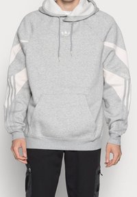 Grå sweatshirt med huva, med vita detaljer, ribbad mudd och kenguruficka. Broderad logotyp på bröstet.